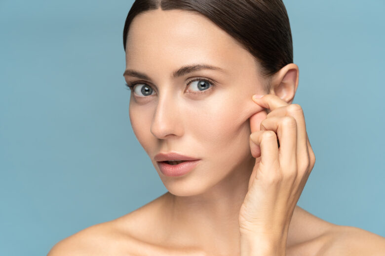 Woman pinches and pulls at face with hand. Her skin is exfoliated and hydrated because she uses Metrin Accelerated Performance System.